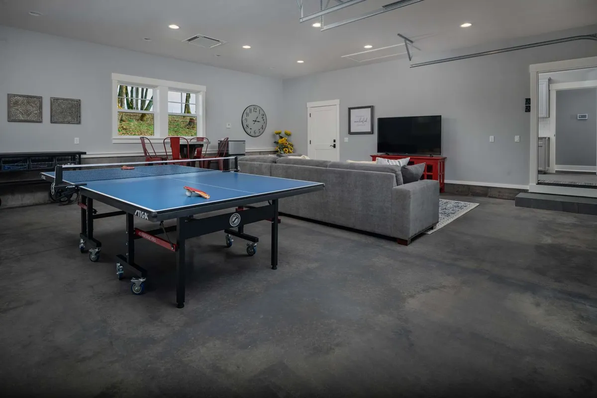 Set in a bright and lively interior, the image centers on a ping pong table, sofa, dining table, television, and wall clock. The layout suggests a flexible space ideal for games, movie nights, and casual gatherings, blending leisure and comfort seamlessly.