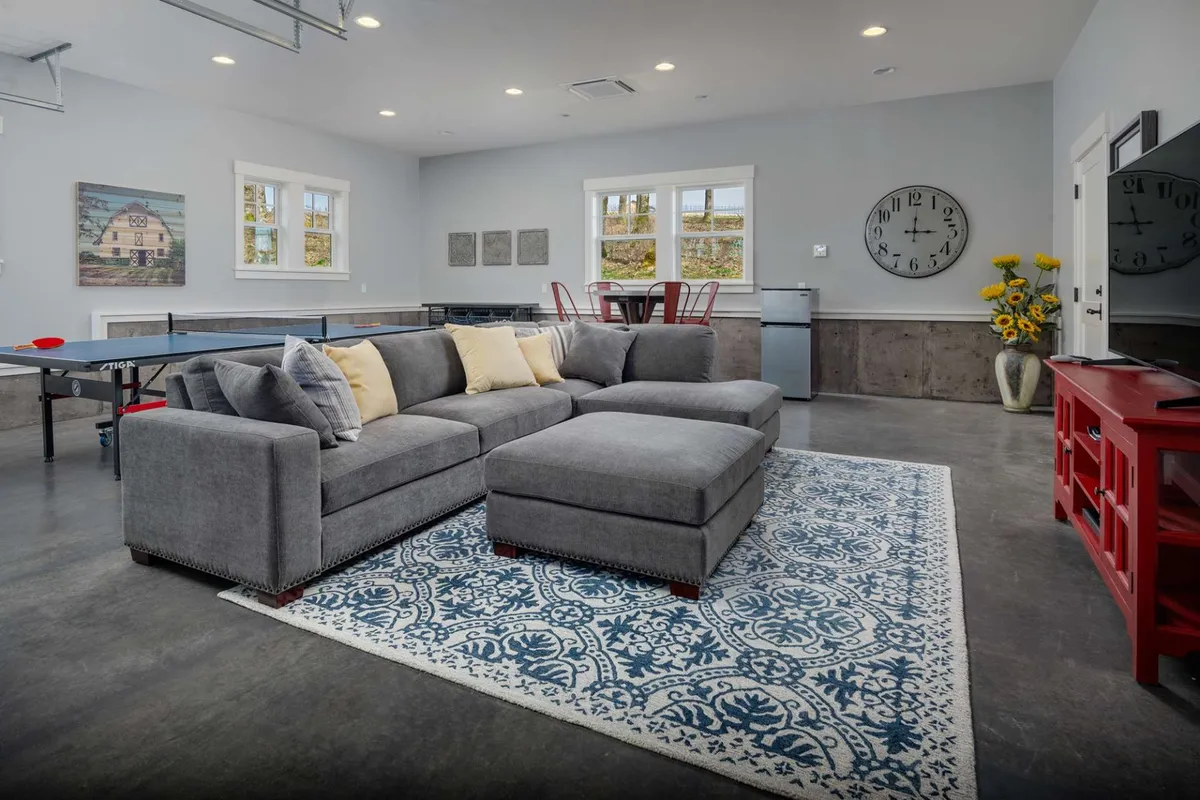 This image reveals a stylish, multi-functional media and game room featuring a gray sectional sofa, a blue decorative rug, a prominent ping pong table at the center, red dining chairs, and curated wall art. The space is arranged for group entertainment, relaxation, and social gatherings, reflecting casual comfort and versatility.