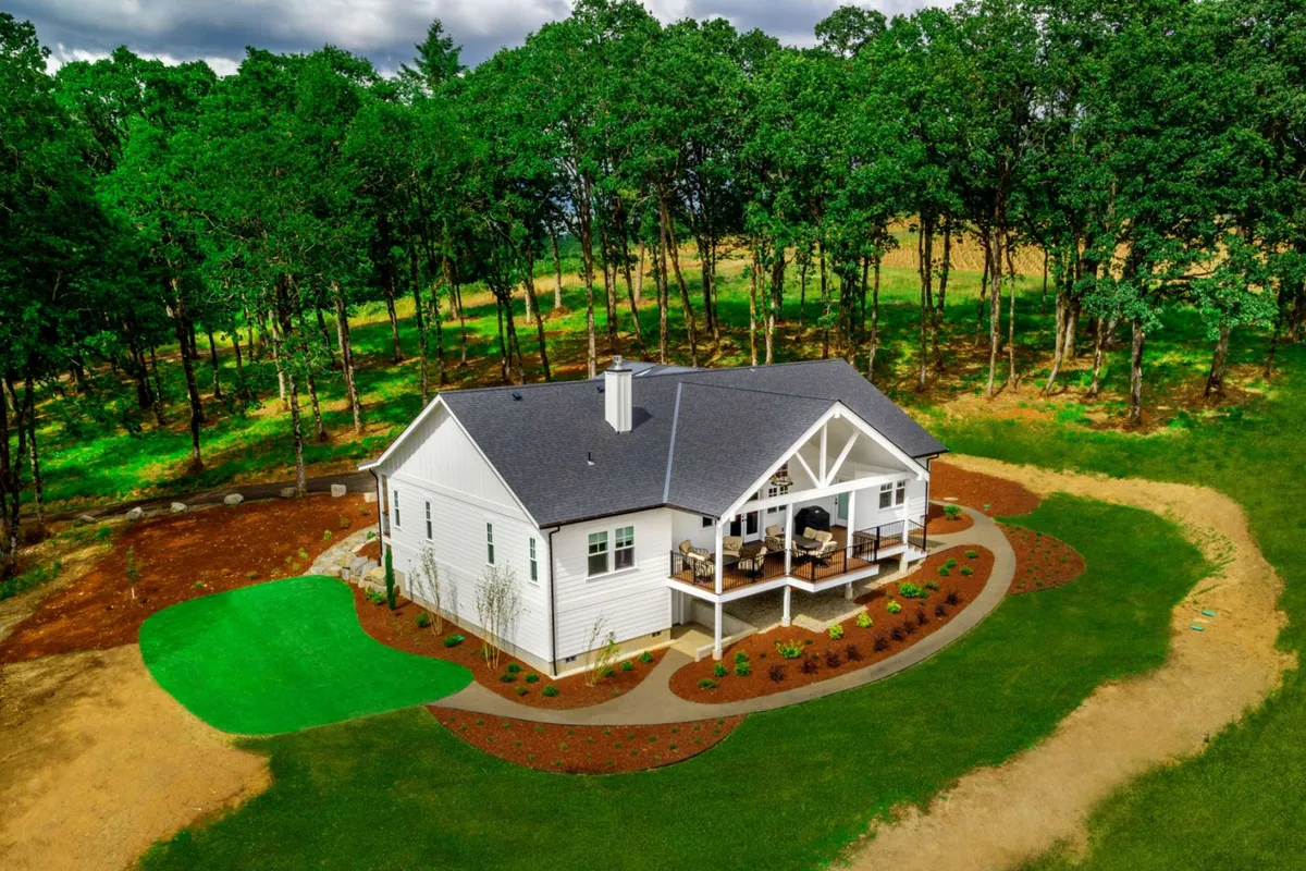 Here, the modern white farmhouse is set within a beautifully landscaped yard, featuring a welcoming outdoor seating area on the porch. The scene feels relaxed and connected to nature—perfect for enjoying a glass of local wine after a day of tasting tours.