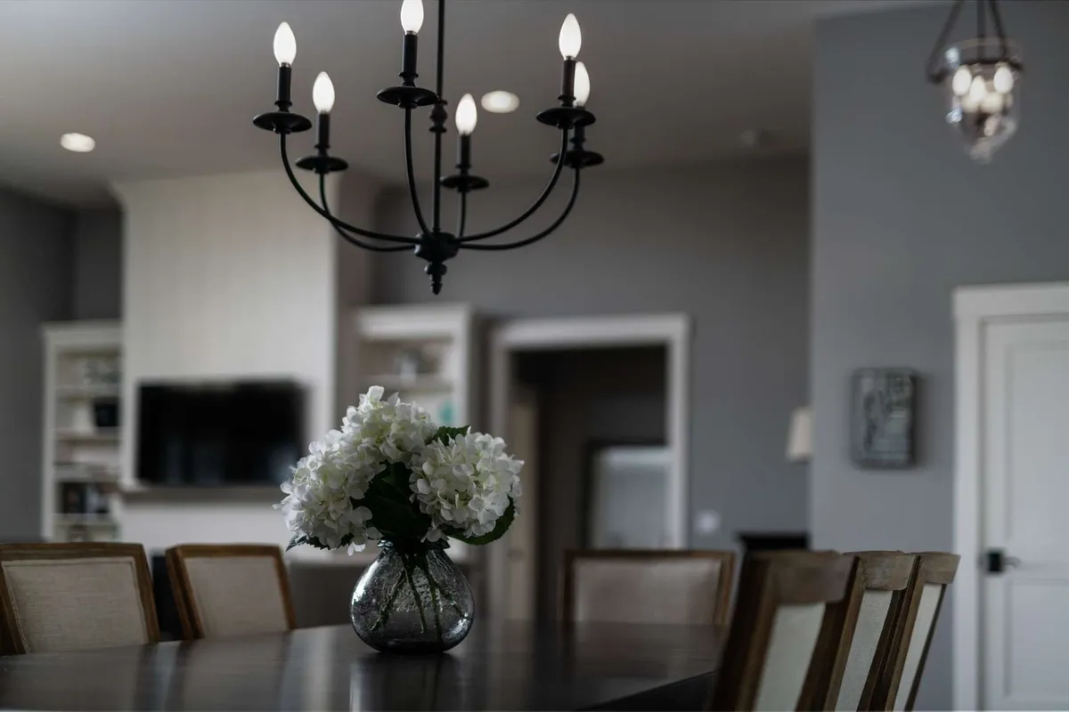 A close-up of a welcoming dining table set beneath a statement chandelier, adorned with fresh flowers as a centerpiece. The setting suggests intimate dinners and joyful gatherings, with tasteful decor reflecting custom finishes.