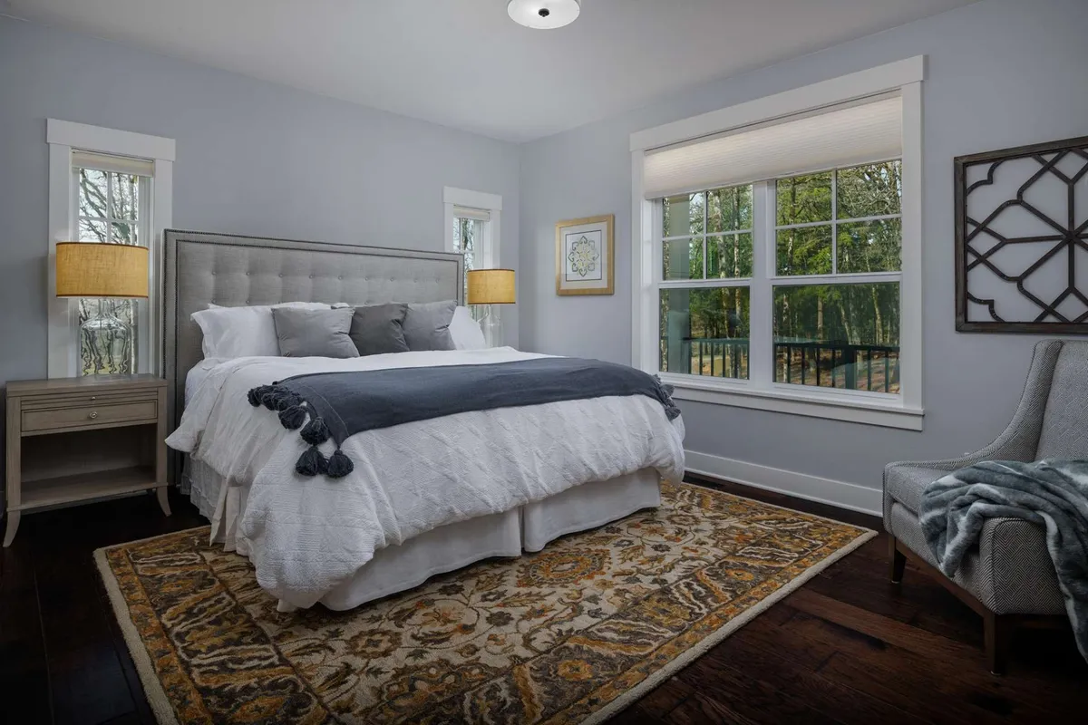 A tranquil bedroom with a plush bed, cozy rug, and large windows that frame vineyard vistas. Comfortable seating by the window creates a serene retreat for relaxation and reading.