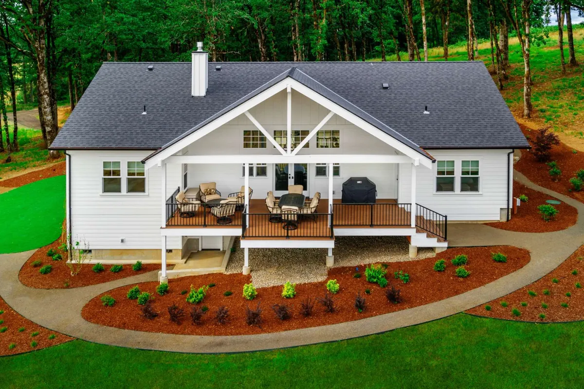 This image captures the front porch and deck area of The Farmhouse, featuring outdoor seating, a lush green lawn, and a welcoming deck that seamlessly connects indoor and outdoor spaces. The open area is surrounded by natural greenery, highlighting the property's expansive grounds and the ideal setting for outdoor dining, relaxation, or watching wildlife at sunset.