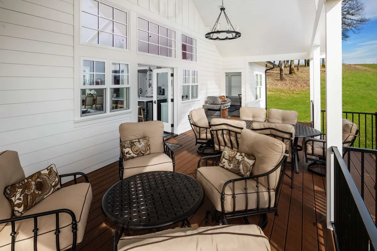 A comfortable outdoor lounge area features plush seating, decorative pillows, and outdoor tables, with a grill area nearby. The scene is set for social gatherings and evening conversations, enhanced by the backdrop of a tranquil, natural setting.