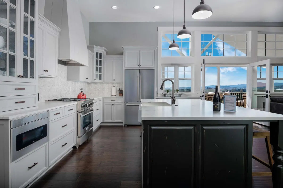 A view of the chef's kitchen featuring a spacious island, gleaming stainless steel appliances, and expansive windows with scenic views. The setup is ideal for cooking, entertaining, and enjoying the interplay of indoor comfort and outdoor beauty.